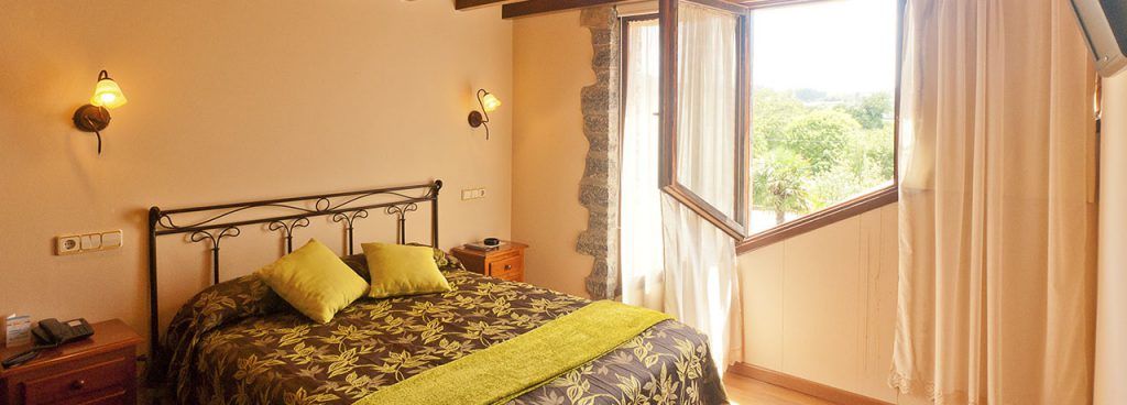 habitación doble estilo moderno donde se ve la cama y vistas de la naturaleza a través de la ventana